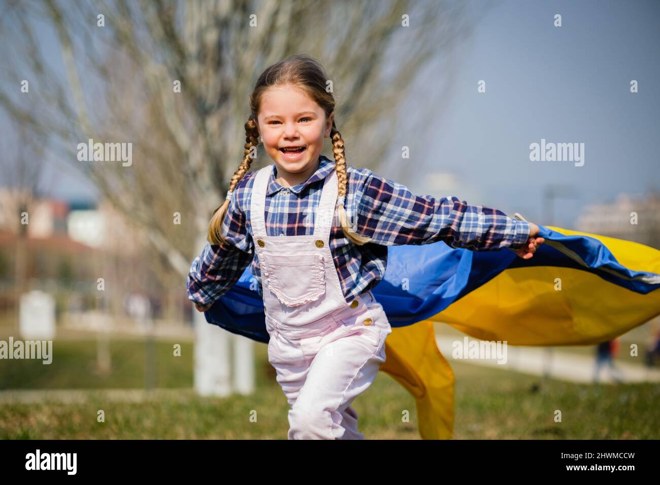 Happy Ukrainian girl running at the park waving the yellow and blue national flag. Concept of love for Ukraine. Independence, flag, Constitution Day Stock Photo