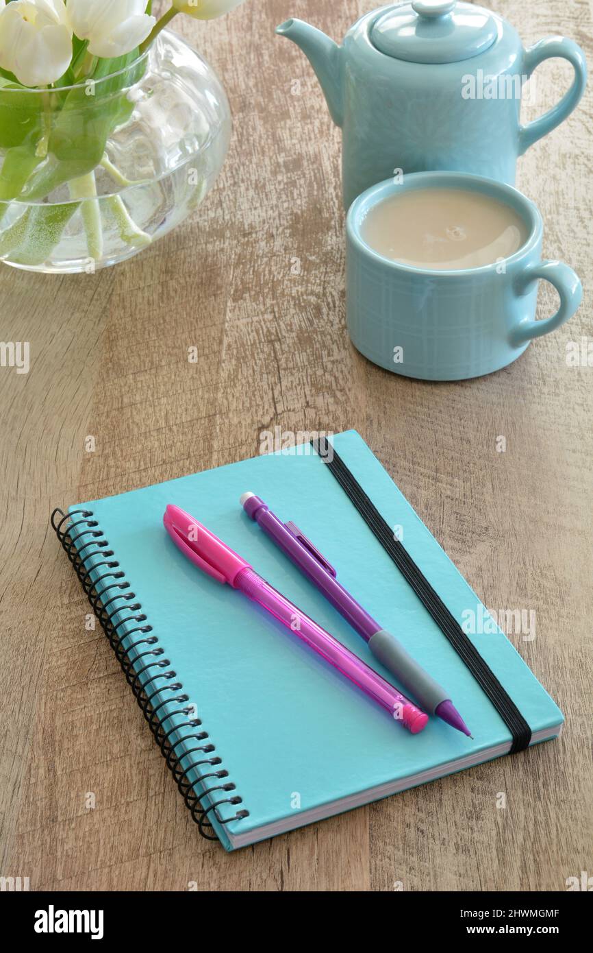 Pen, pencil and notebook setup for writing. Tea and white tulips create