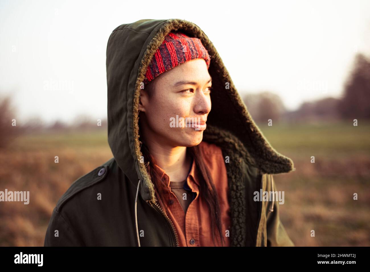 Non-binary person smiles in afternoon sun outdoors in field with hood Stock Photo