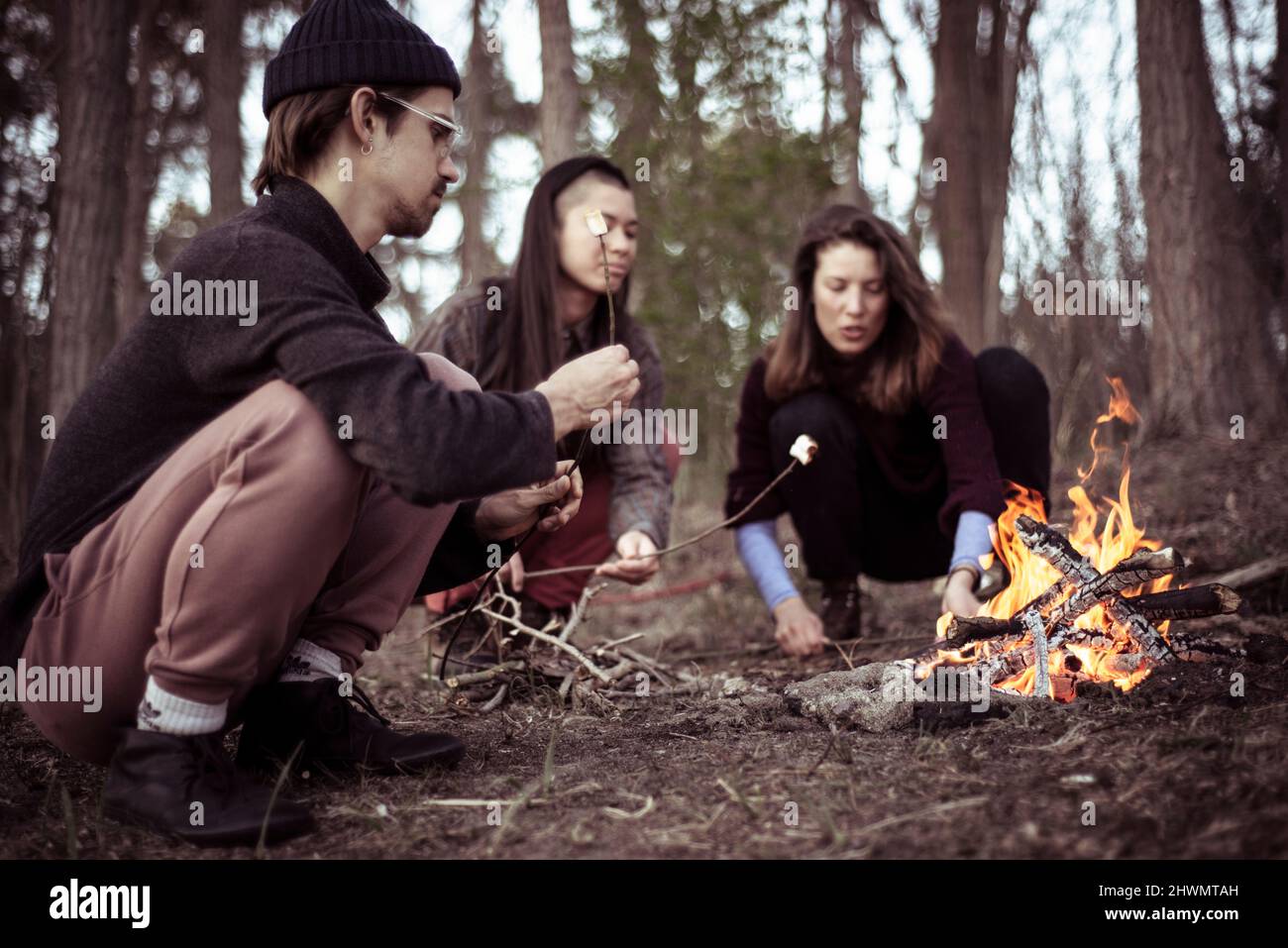 alternative friends gather and squat to roast marshmallows by fire Stock Photo