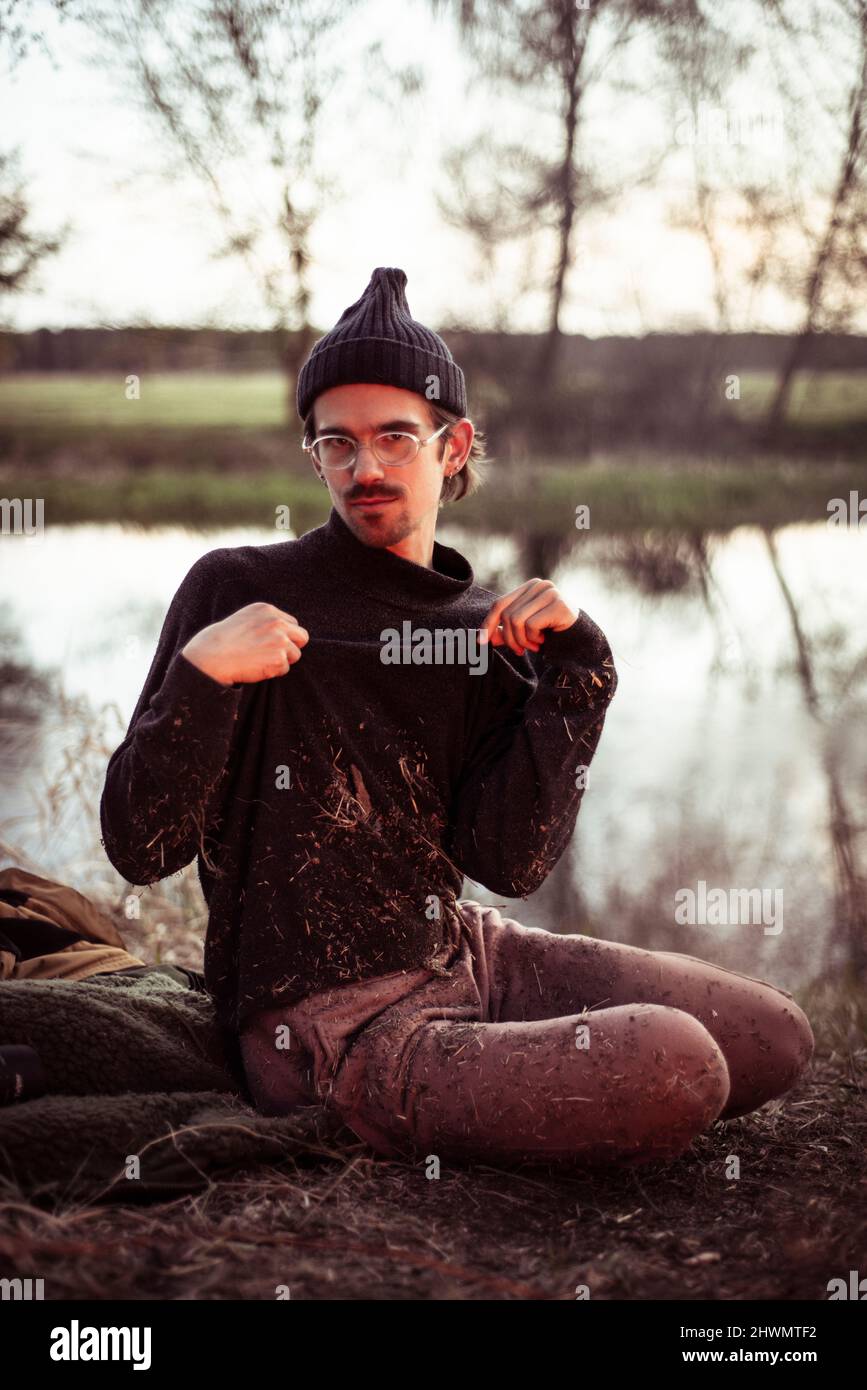 young alternative man poses with grass on clothes by water and fire Stock Photo