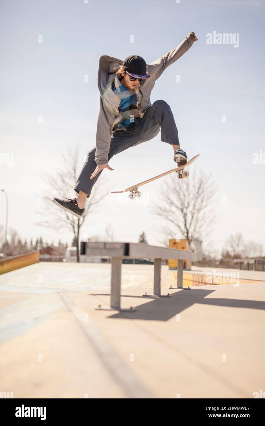 Young skateboard enthusiast in skatepark jumping over bench Stock Photo