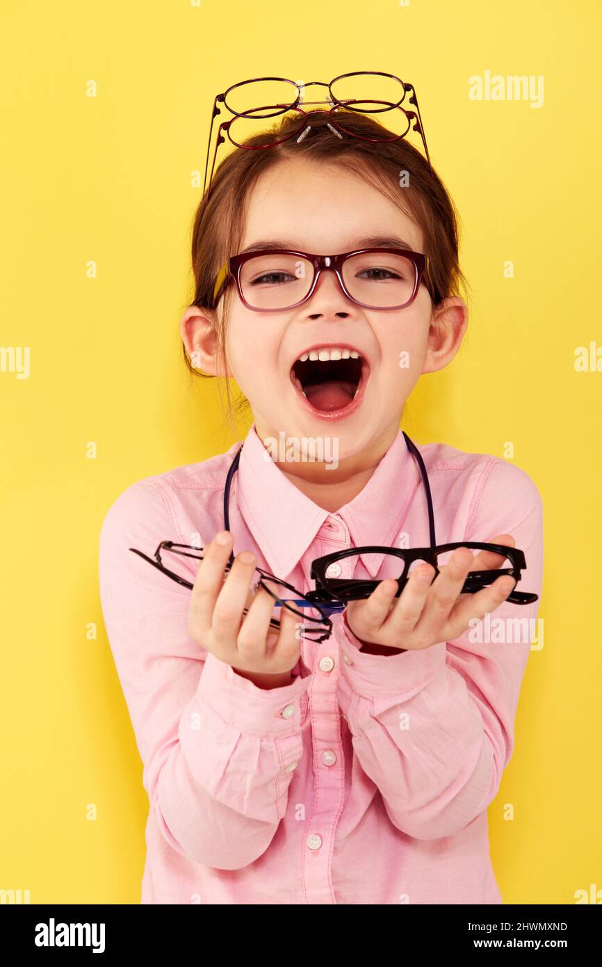 Shes excited about spectacles. A cute little girl standing against a yellow background with a hand full of glasses. Stock Photo