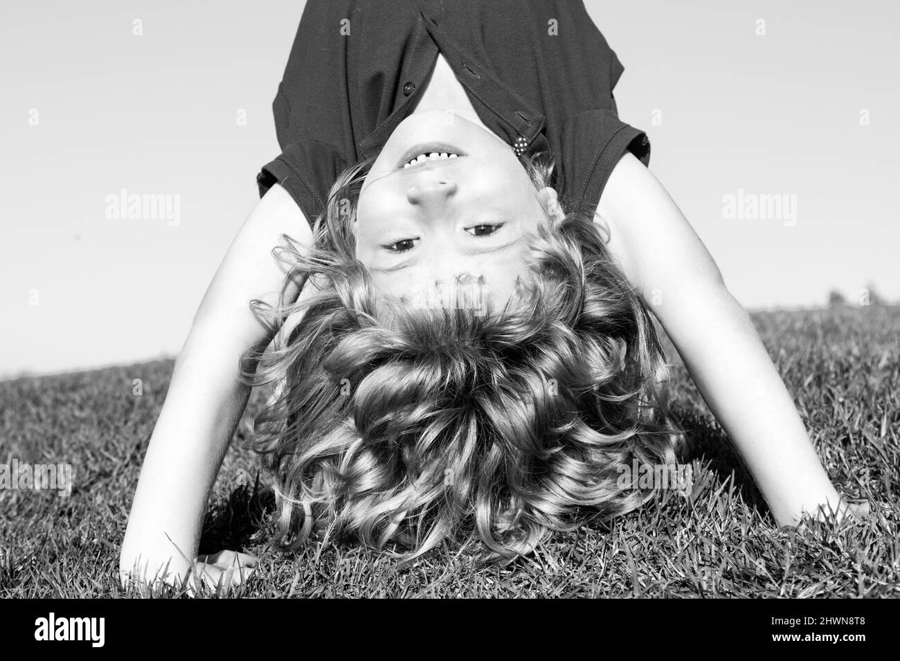 Portrait of a happy smiling child boy playing upside down on grass field outdoor. Laughing child. Expressive facial expressions. Stock Photo