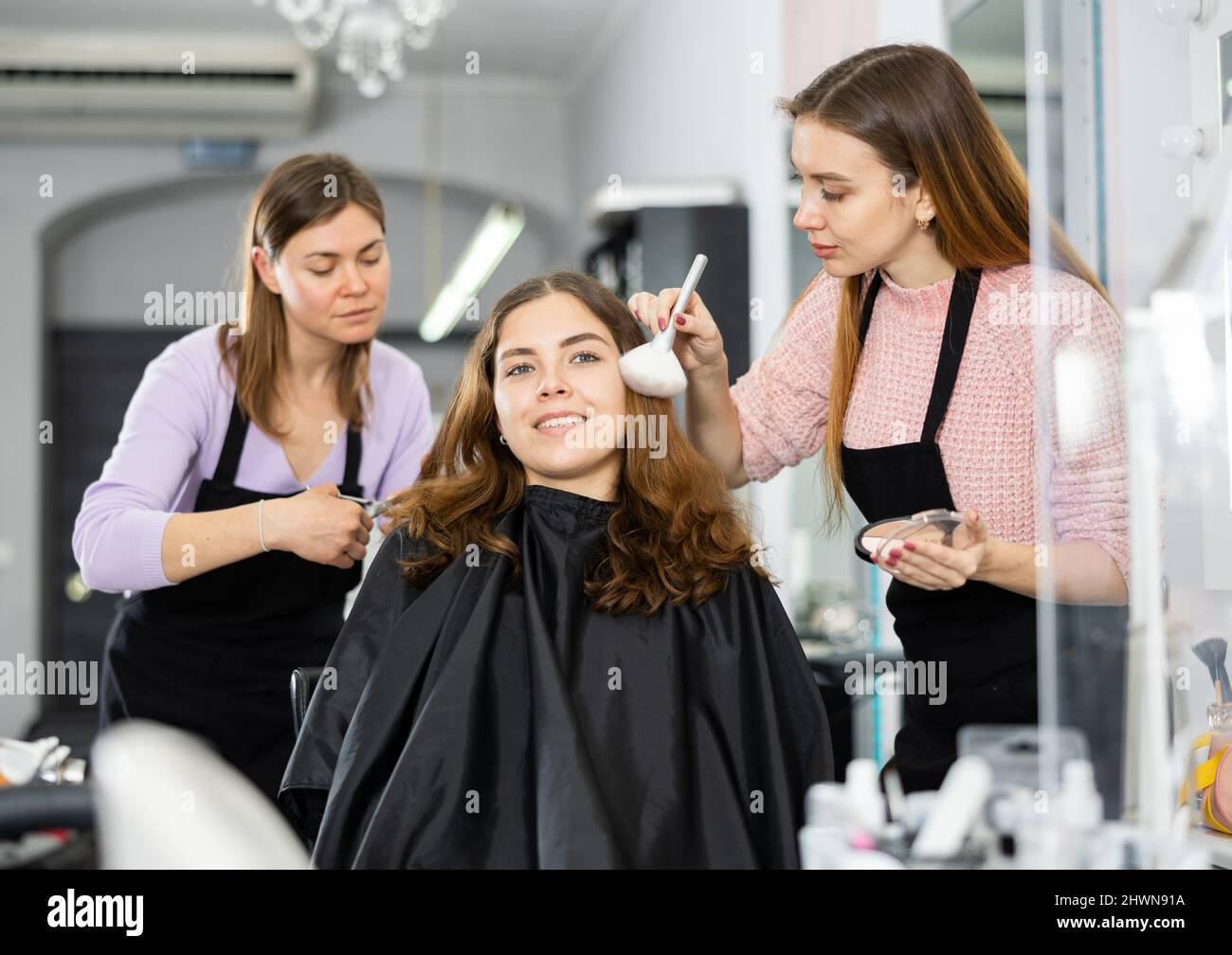 Makeup artist and a hairdresser serve a young female client Stock