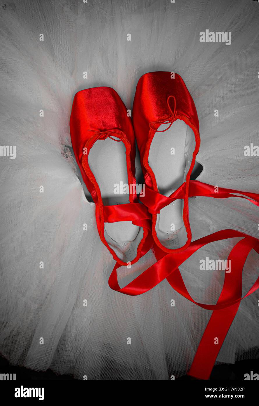 Red ballet pointe shoes set on top of a white tutu. Stock Photo
