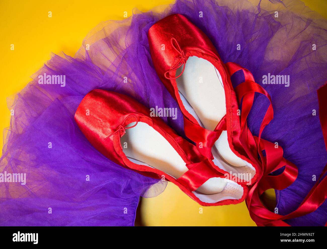 Red ballet pointe shoes set on top of a purple tutu, and a yellow background. Stock Photo