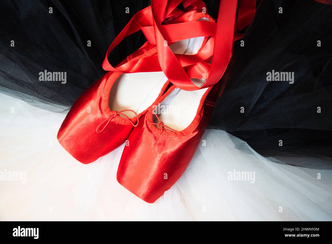Red ballet pointe shoes resting on a white and black tutu. Stock Photo