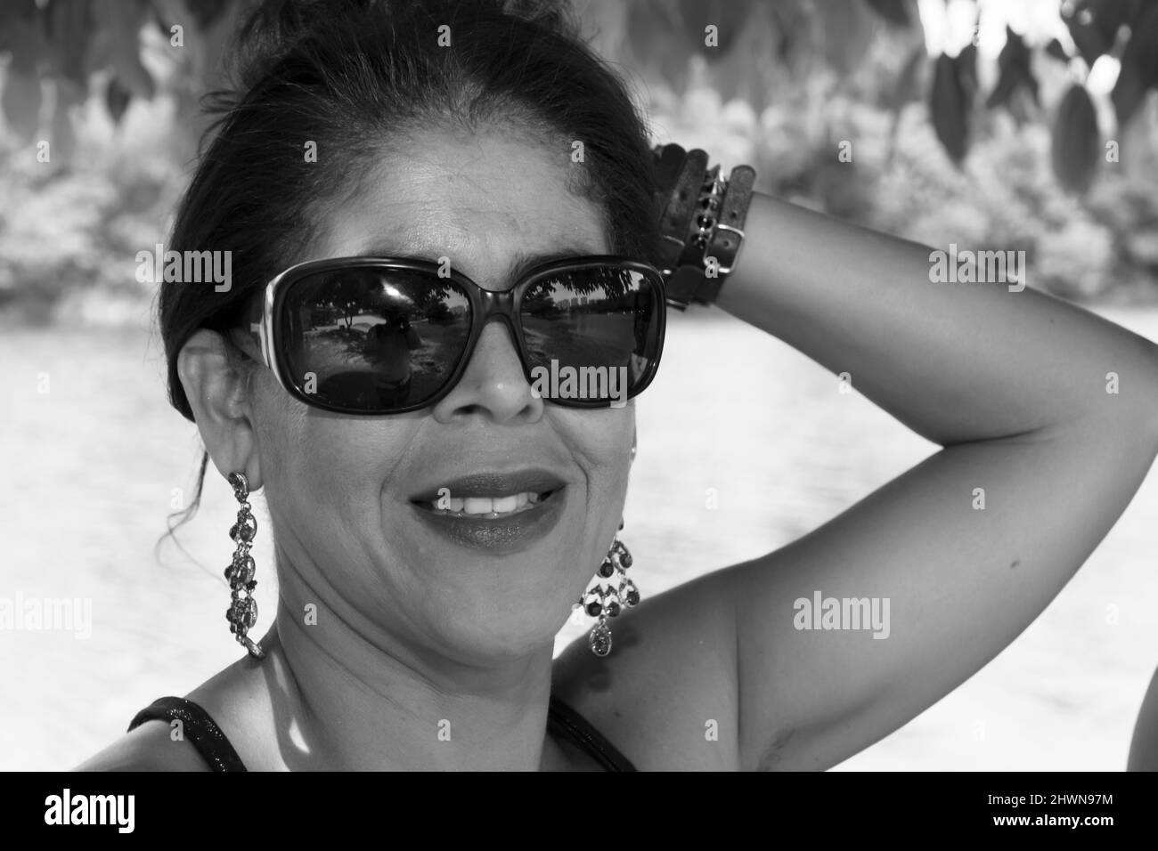 Close-up portrait of a woman wearing sunglasses against a river with trees in the background. Salvador, Bahia, Brazil. Stock Photo
