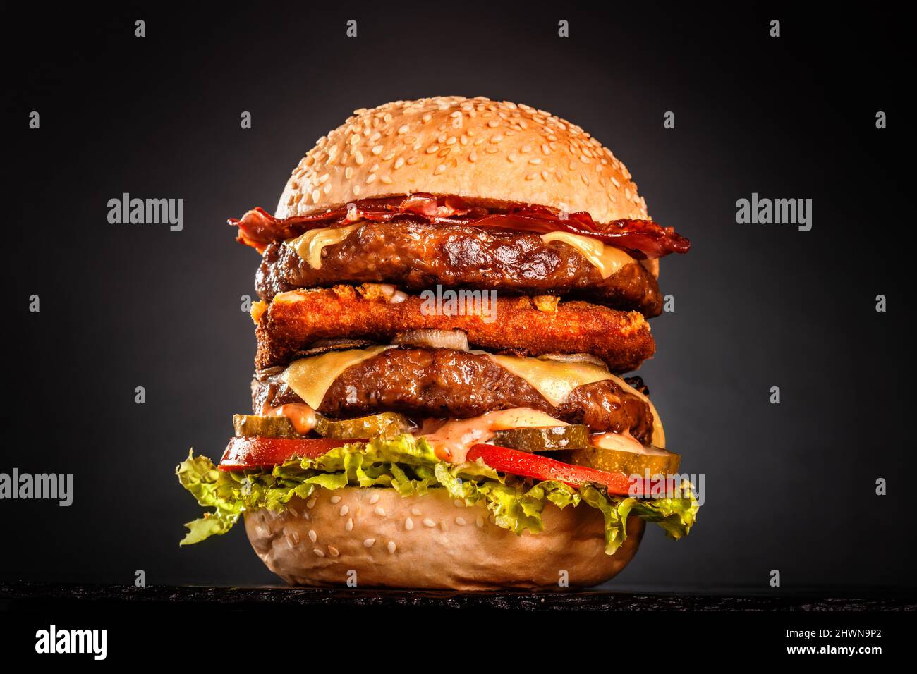 Double burger with bacon grilled yellow cheese onions tomatoes cucumber and lettuce. Isolated on black background. Stock Photo