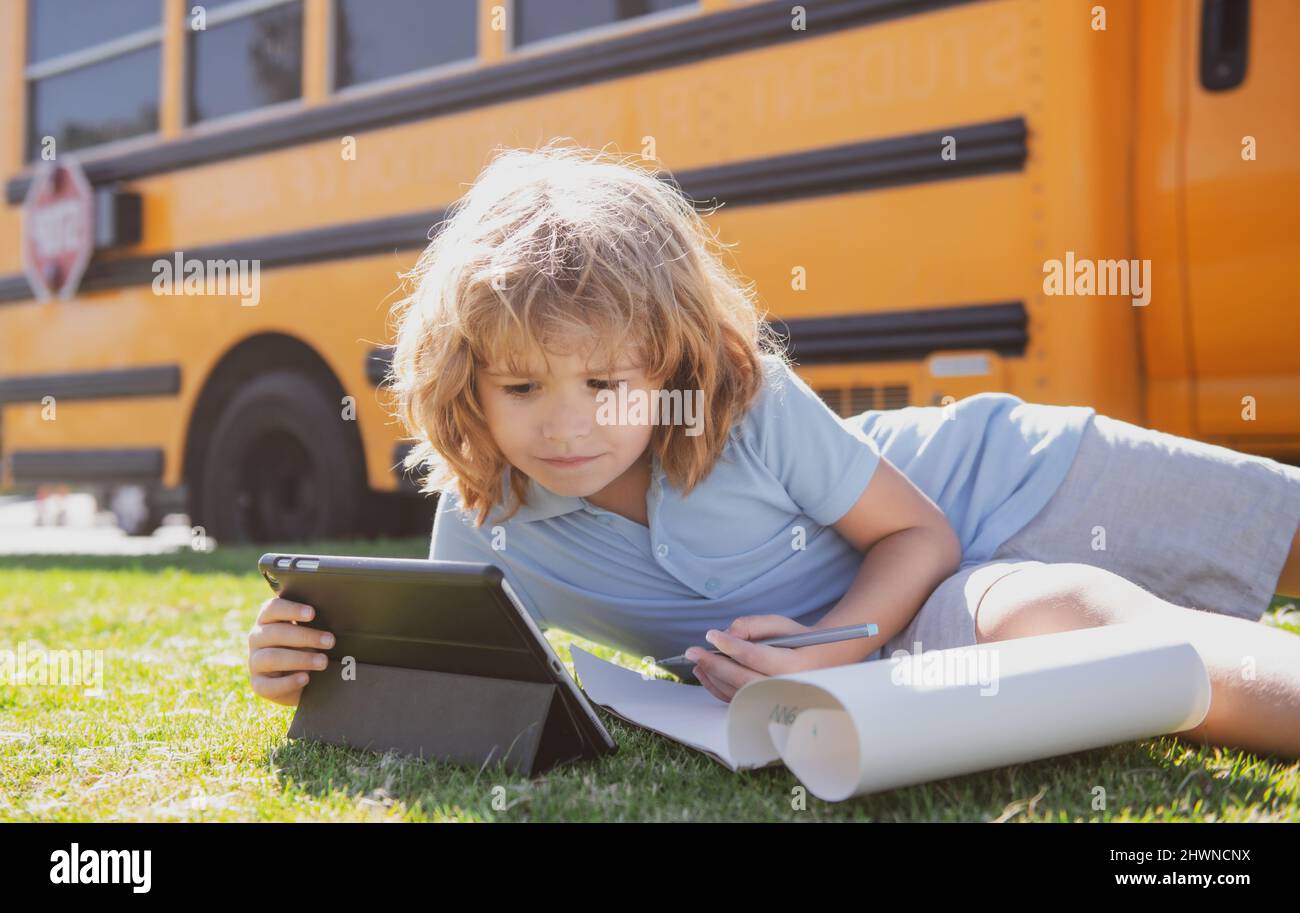 Pupil writing homework on grass with laptop outdoor near school bus ...