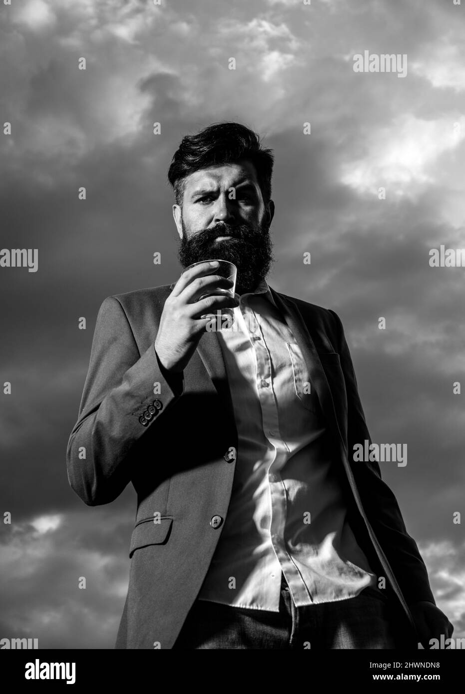 Hipster male with stylish beard drinking cognac, vodka or brandy. Fashion Luxury rich bearded man drink expensive beverage. Stock Photo