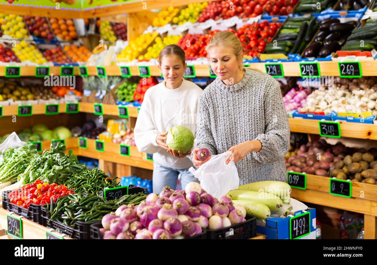Portrait of teenage girl and her mother who buying fresh vegetables and ...