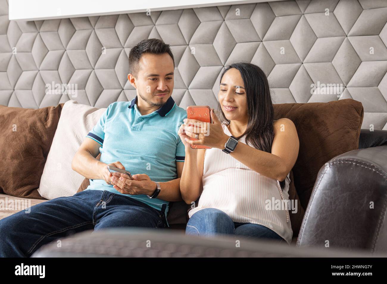Couple of man and pregnant woman smiling using their smart phone in the living room of their house Stock Photo