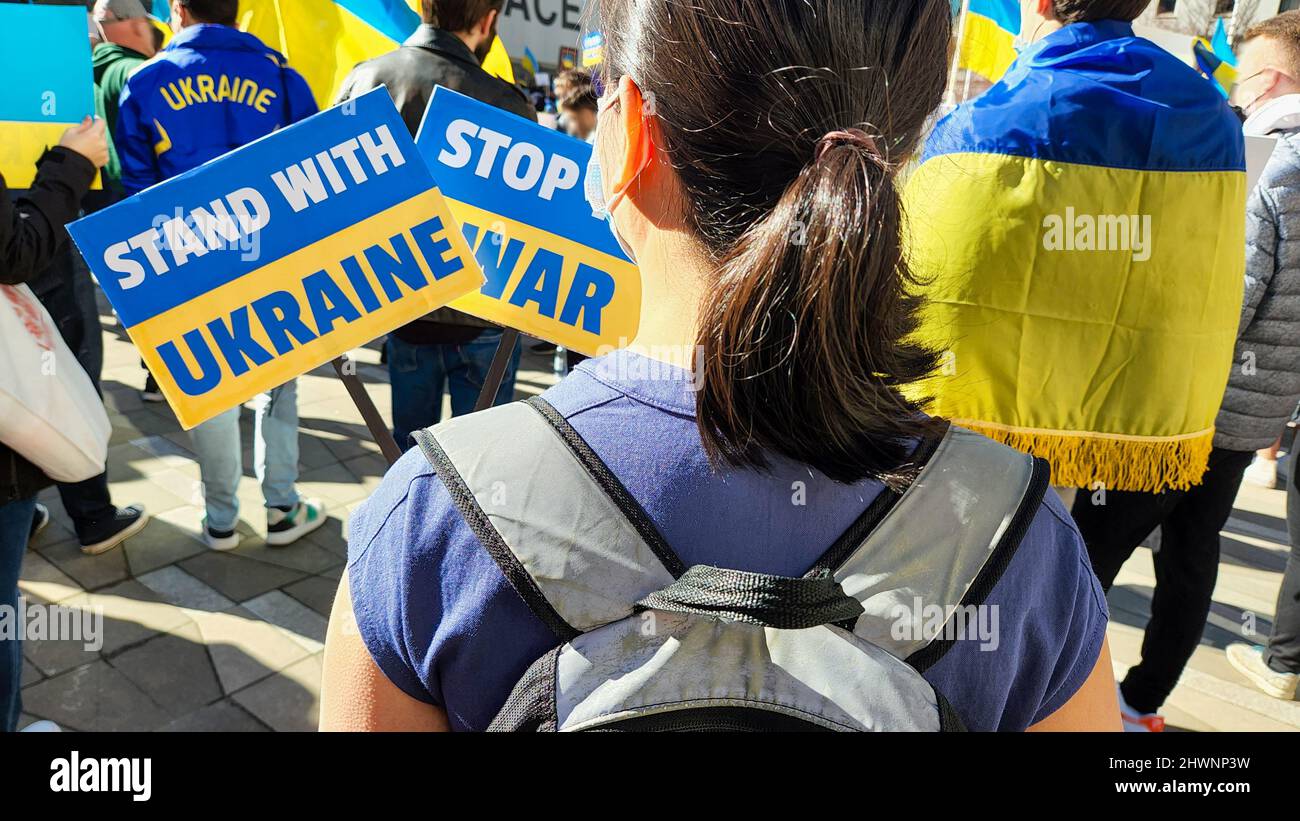 at a political rally against the war, a girl stands in the crowd and holds banners with the inscription stop the war and stand with Ukraine, a man wit Stock Photo