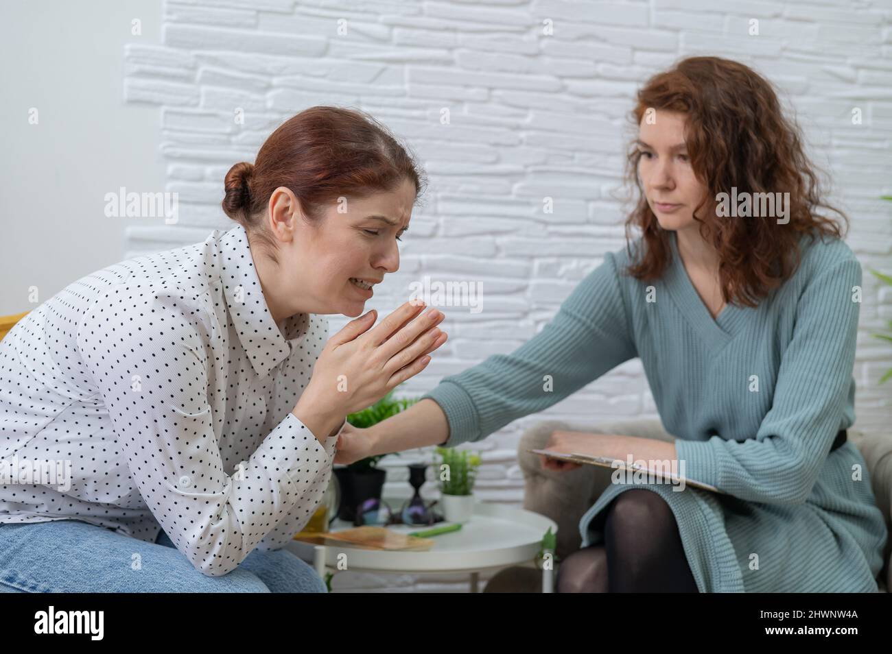 Caucasian woman crying at psychotherapy session. The female doctor calms the patient and holds her hand. Stock Photo