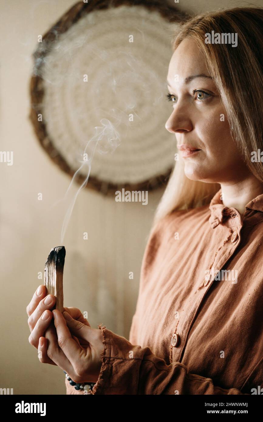 Woman meditating with palo santo in studio, cleaning space with smoke. Adult person using burning spiritual incenses at home Stock Photo