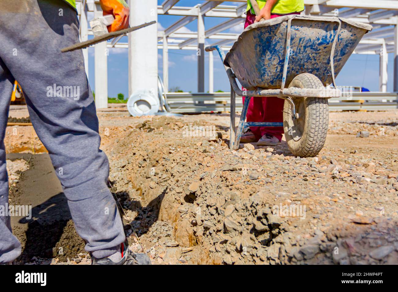 Construction worker is using shovel to unloading cement from wheelbarrow on construction site. Stock Photo