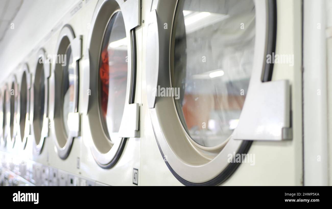 Row of washing and drying machines, public coin laundry in California, USA. Drums of washers and dryers in self-service laundromat or commercial laundrette. Automatic launderette in United States. Stock Photo