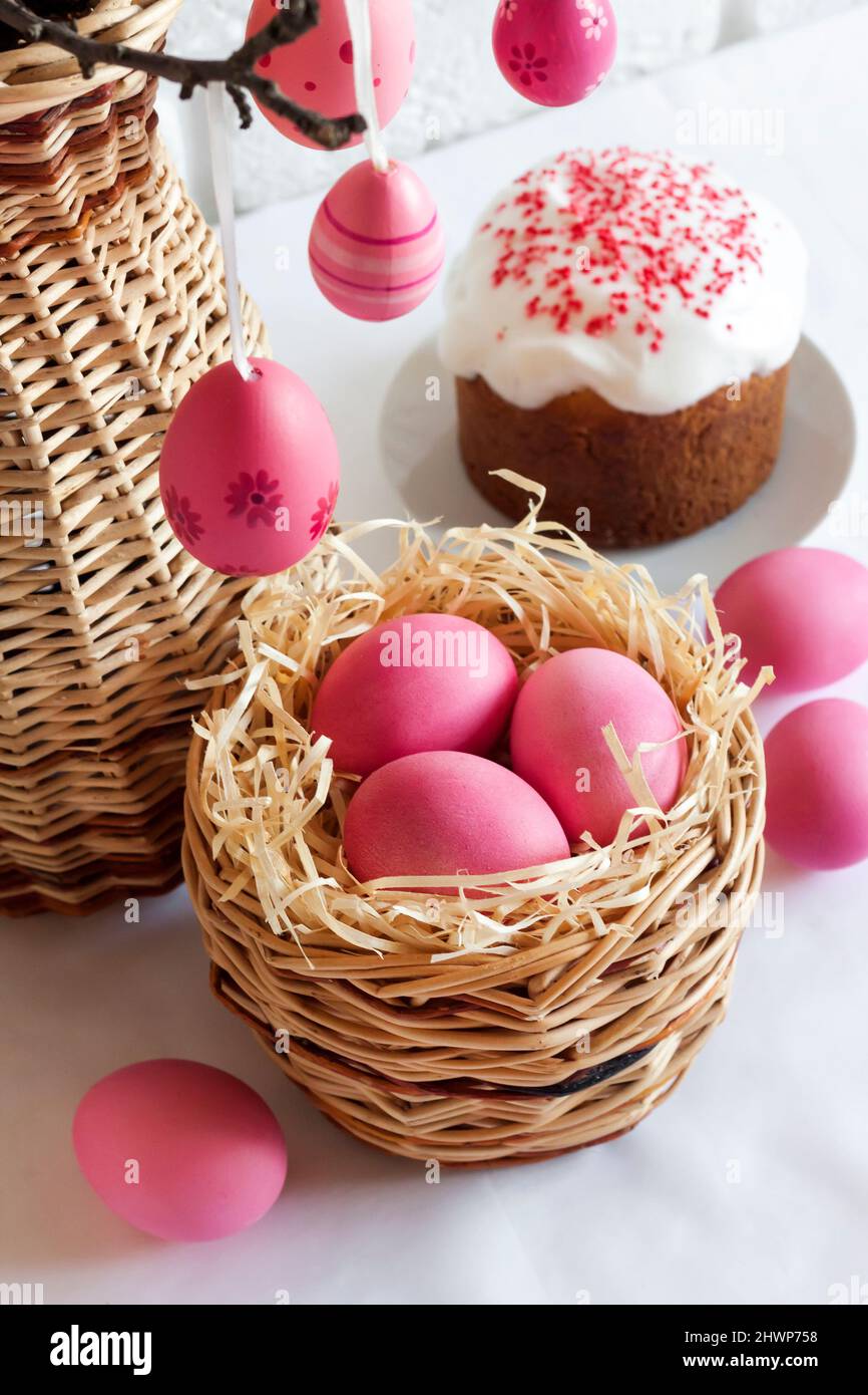 Easter composition with pink colored eggs in wicker basket and Easter cake on white background Stock Photo