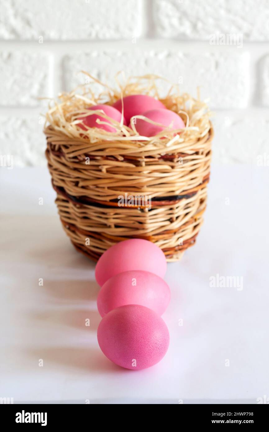 Minimalistic Easter composition with wicker basket and pink colored eggs on white background Stock Photo