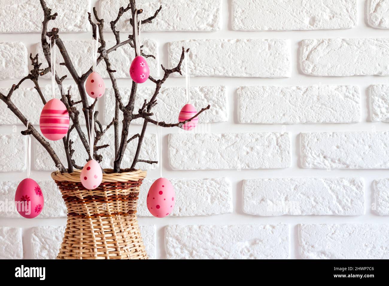 Easter composition with tree branches in a wicker vase decorated with pink colored eggs  on white background. Copy space Stock Photo