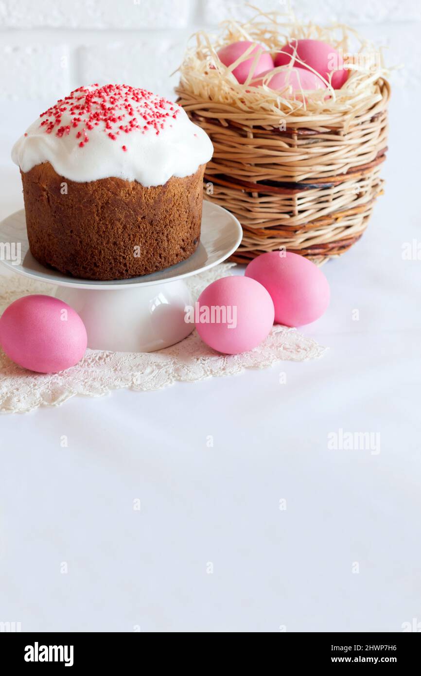 Minimalistic Easter composition with wicker basket with pink colored eggs and Easter cake on white background. Copy space Stock Photo