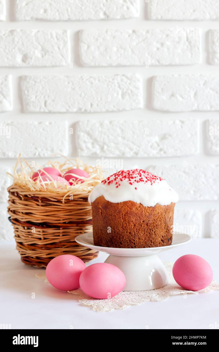 Minimalistic Easter composition with wicker basket with pink colored eggs and Easter cake on white background. Copy space Stock Photo