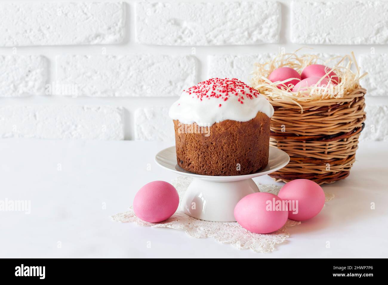 Minimalistic Easter composition with wicker basket with pink colored eggs and Easter cake on white background. Copy space Stock Photo