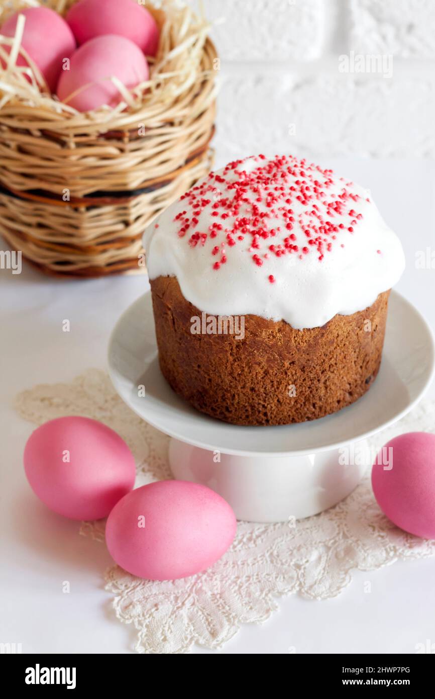 Minimalistic Easter composition with wicker basket with pink colored eggs and Easter cake on white background Stock Photo