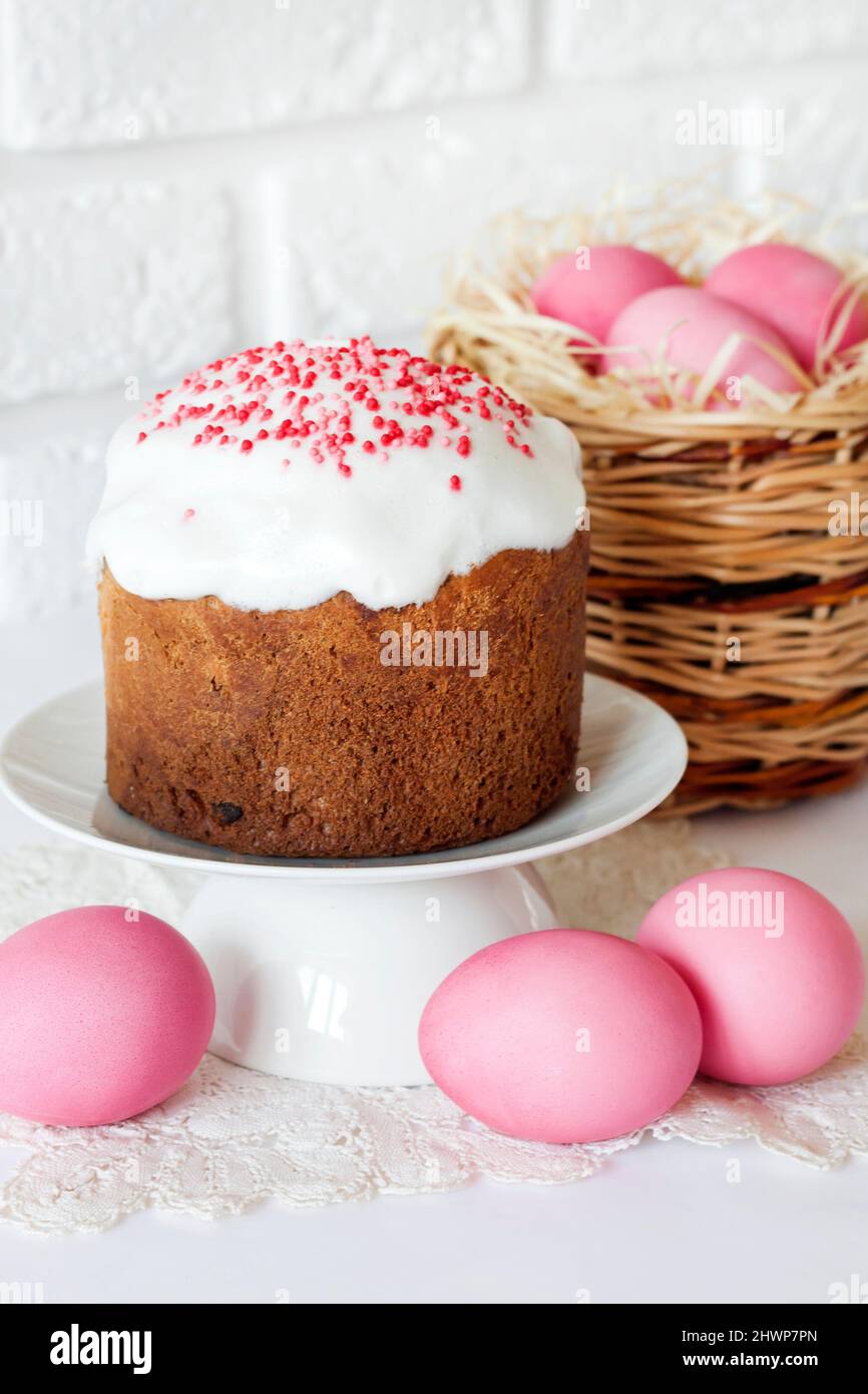 Minimalistic Easter composition with wicker basket with pink colored eggs and Easter cake on white background Stock Photo
