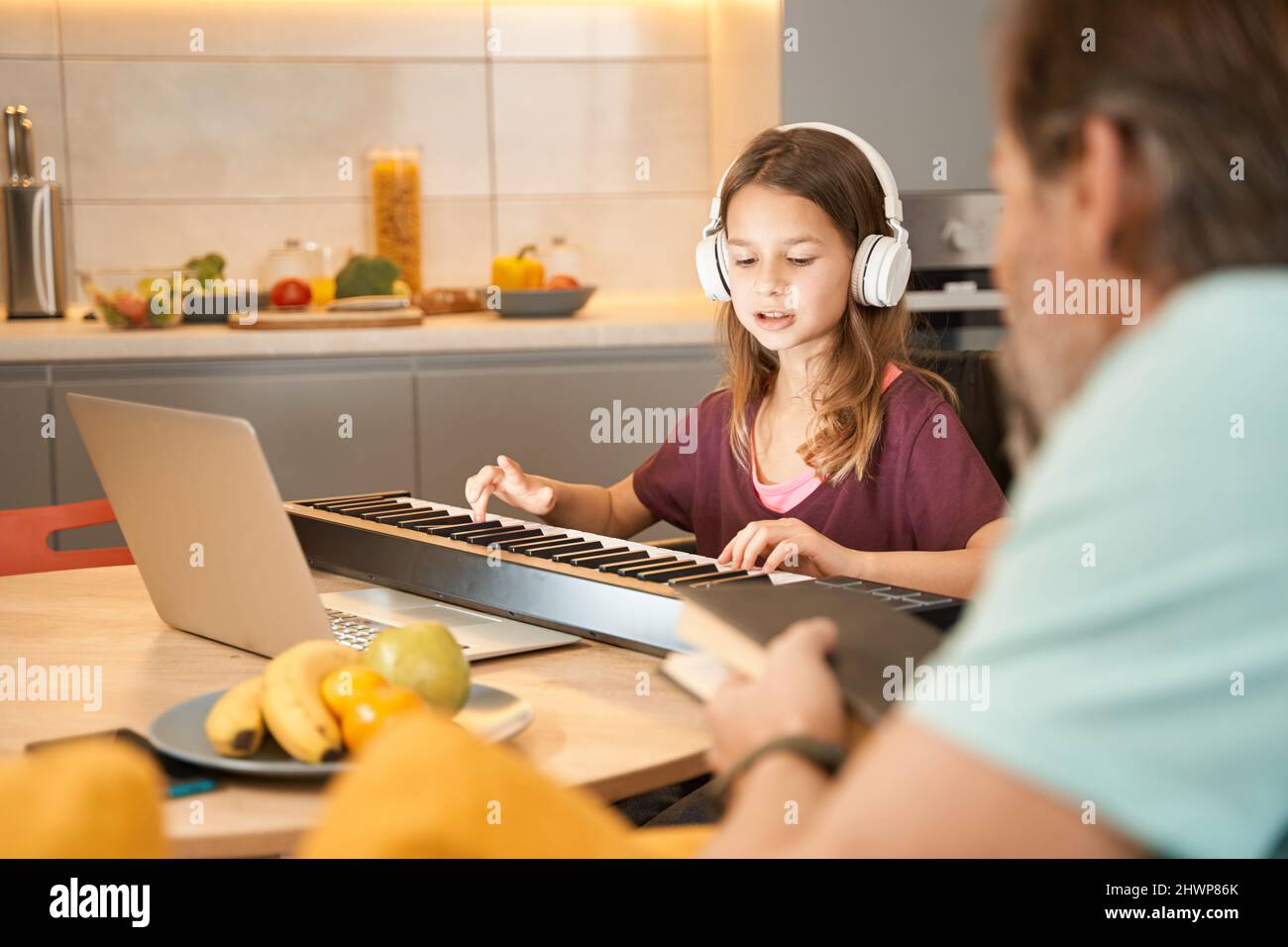 Teenage girl learning to play synthesizer with father in kitchen Stock