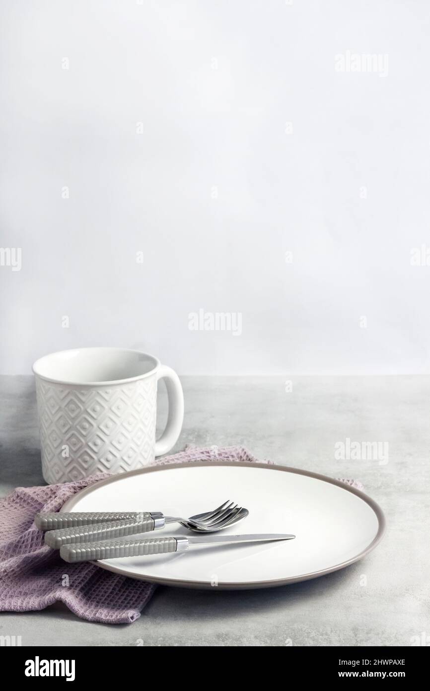 Table setting. White plate, mug, cutlery and napkin on light gray background. Stock Photo