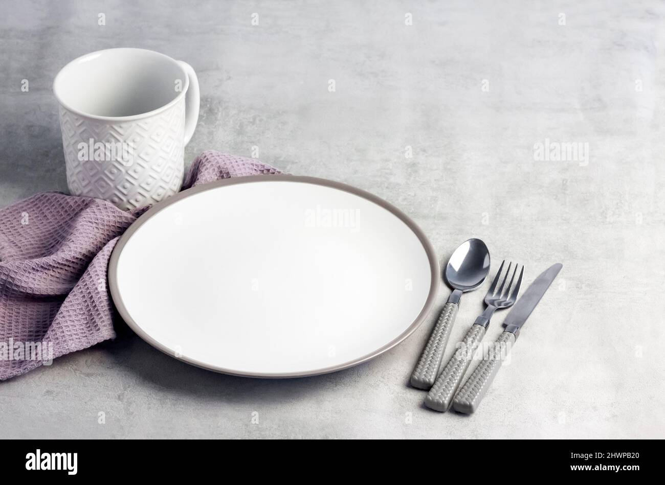 Table setting. White plate, mug, cutlery and napkin on light gray background. Stock Photo