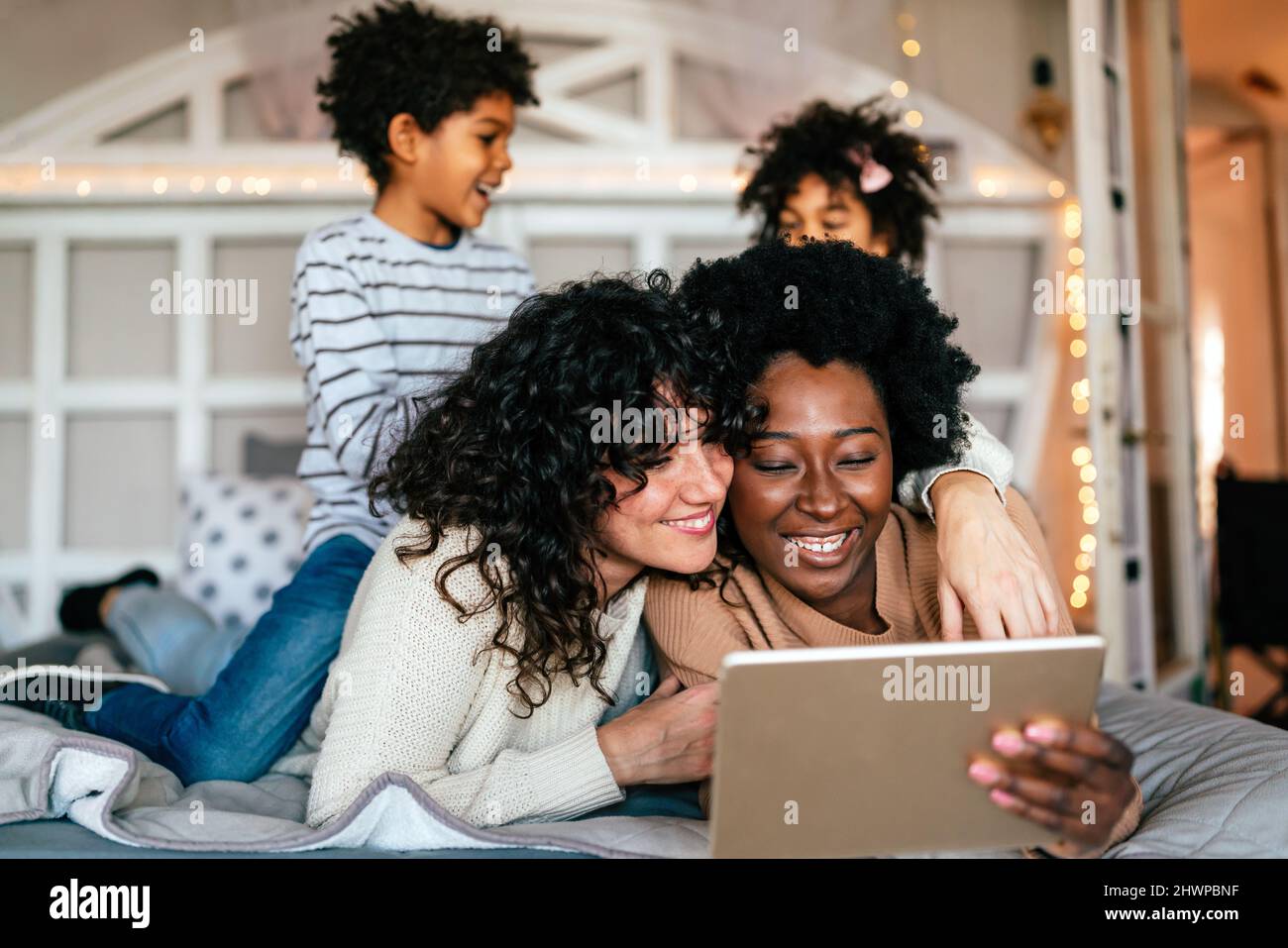 Happy gay couple looking at digital tablet and having fun with children together at home Stock Photo