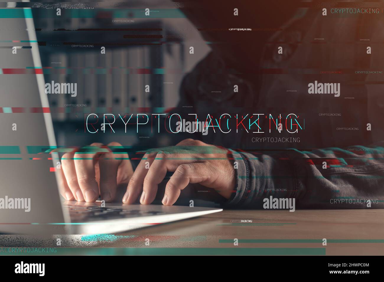 Cryptojacking concept with faceless hooded hacker working on laptop computer, with glitch effect and selective focus Stock Photo