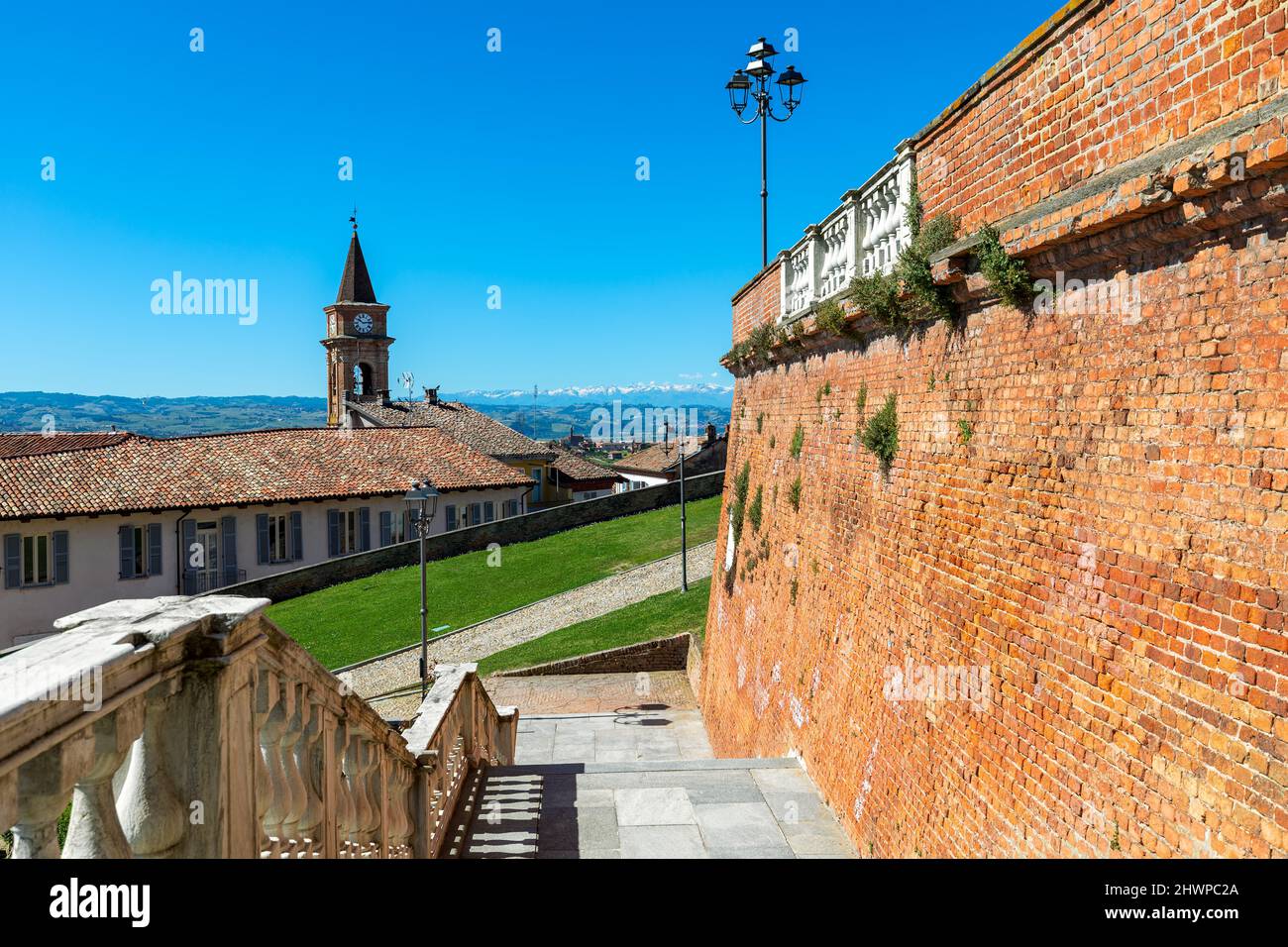 View of old brick wall, houses and belfry under blue sky in small town of Govone in Piedmont, Northern Italy. Stock Photo