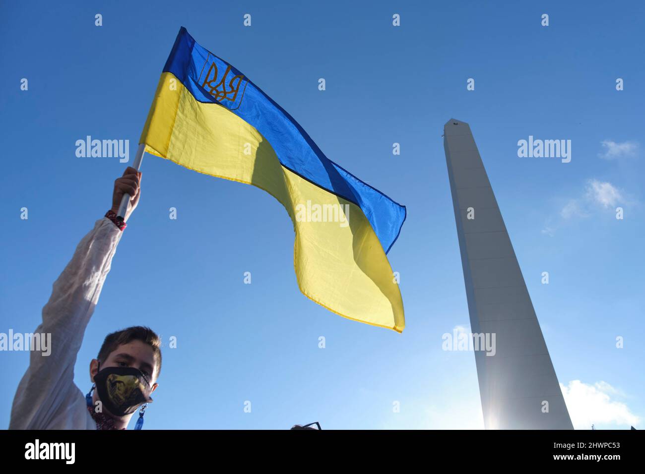 Buenos Aires, Argentina; March 6, 2022: march for peace in Ukraine, against Russian war and invasion. Young boy raises an Ukrainian flag next to the o Stock Photo