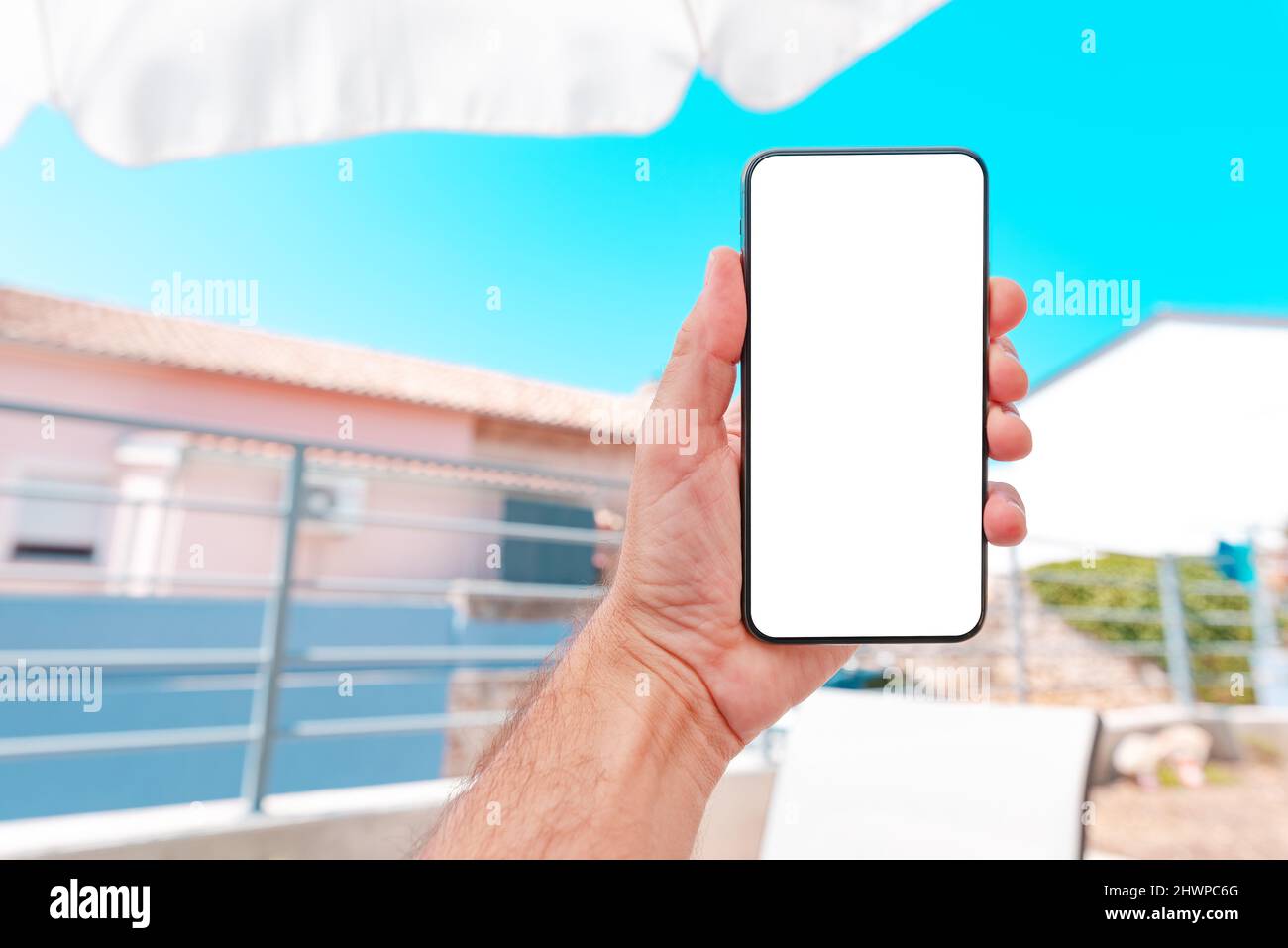Mobile smart phone mockup screen, man enjoying summer vacation at apartment terrace and holding device, close up with selective focus Stock Photo