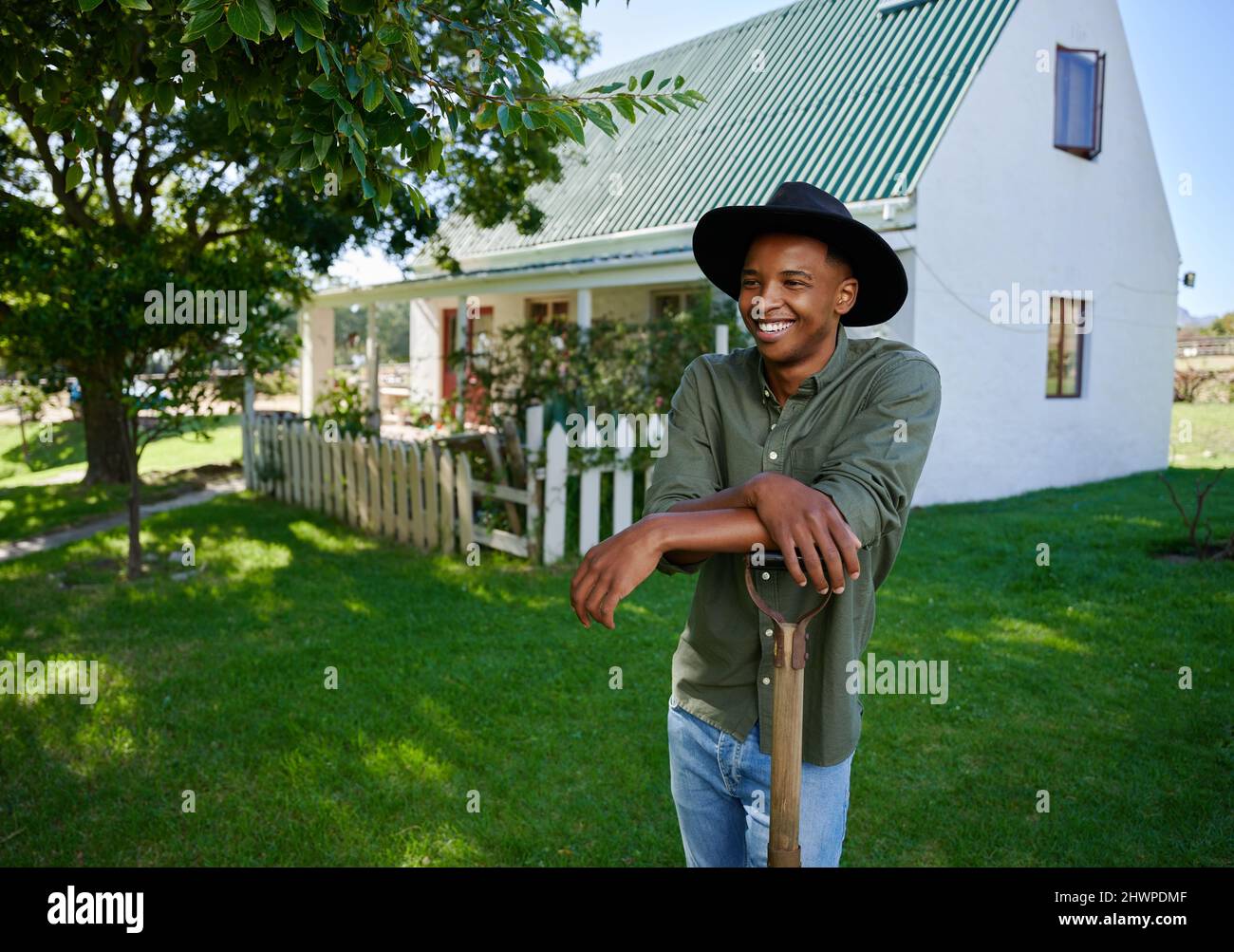 Mixed race farmer standing in green fields leaning on pitchfork Stock Photo