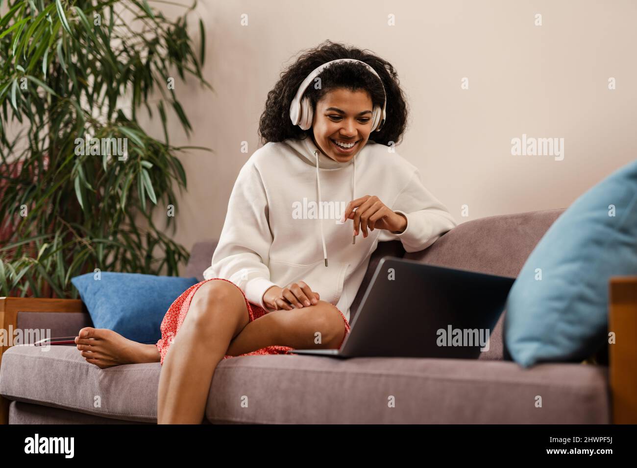 Young black woman in headphones using laptop while sitting on sofa at ...