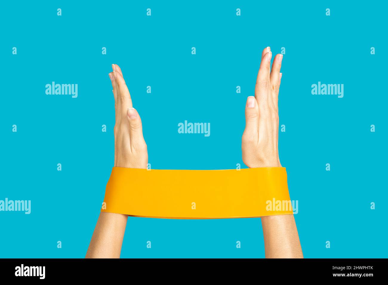 Closeup of isolated hands exercising with orange resistance band on blue background. Doing physical activities to keep feet. Getting fit at home by Stock Photo