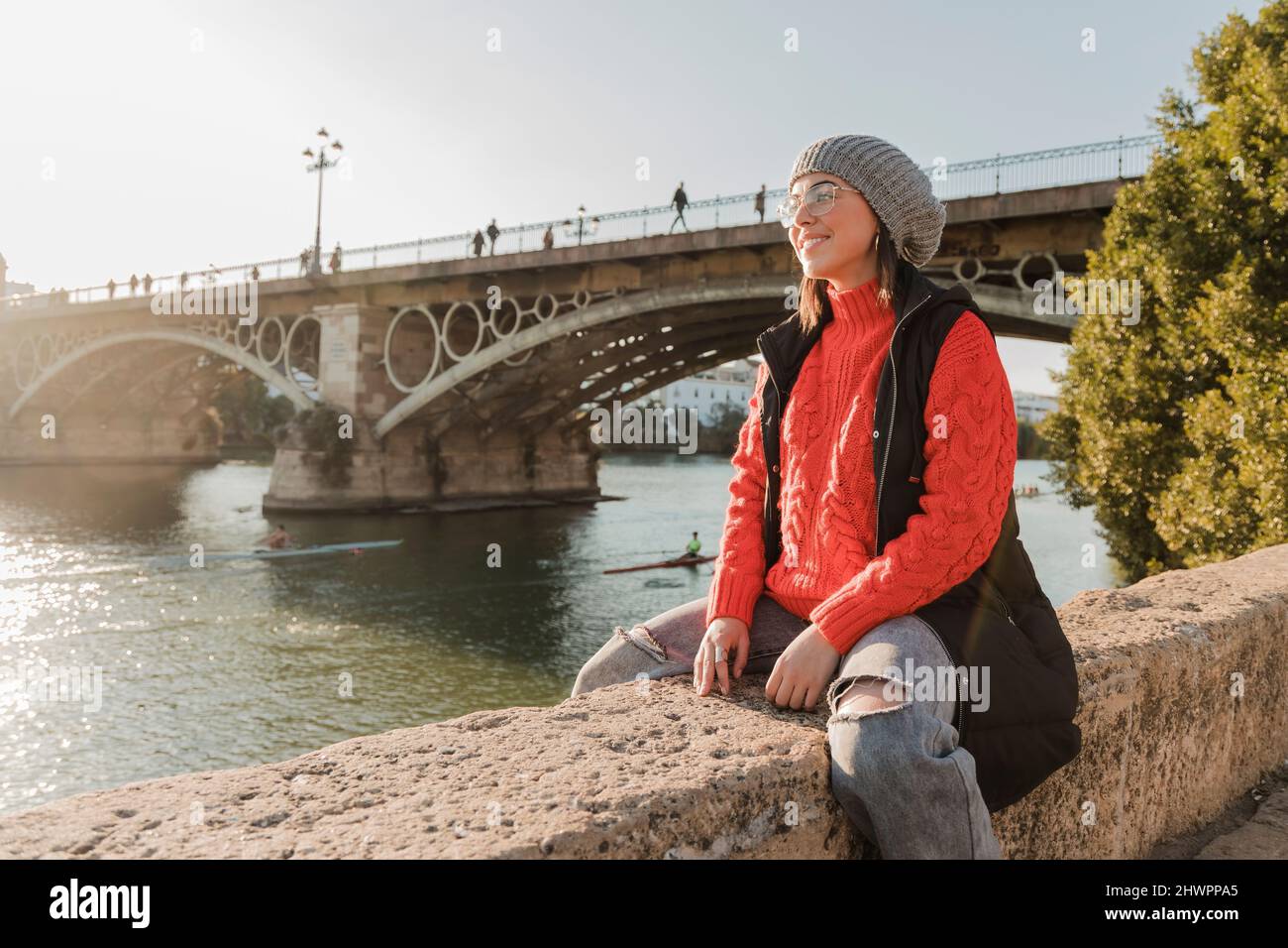 Happy woman sitting in front of bridge at riverbank Stock Photo - Alamy