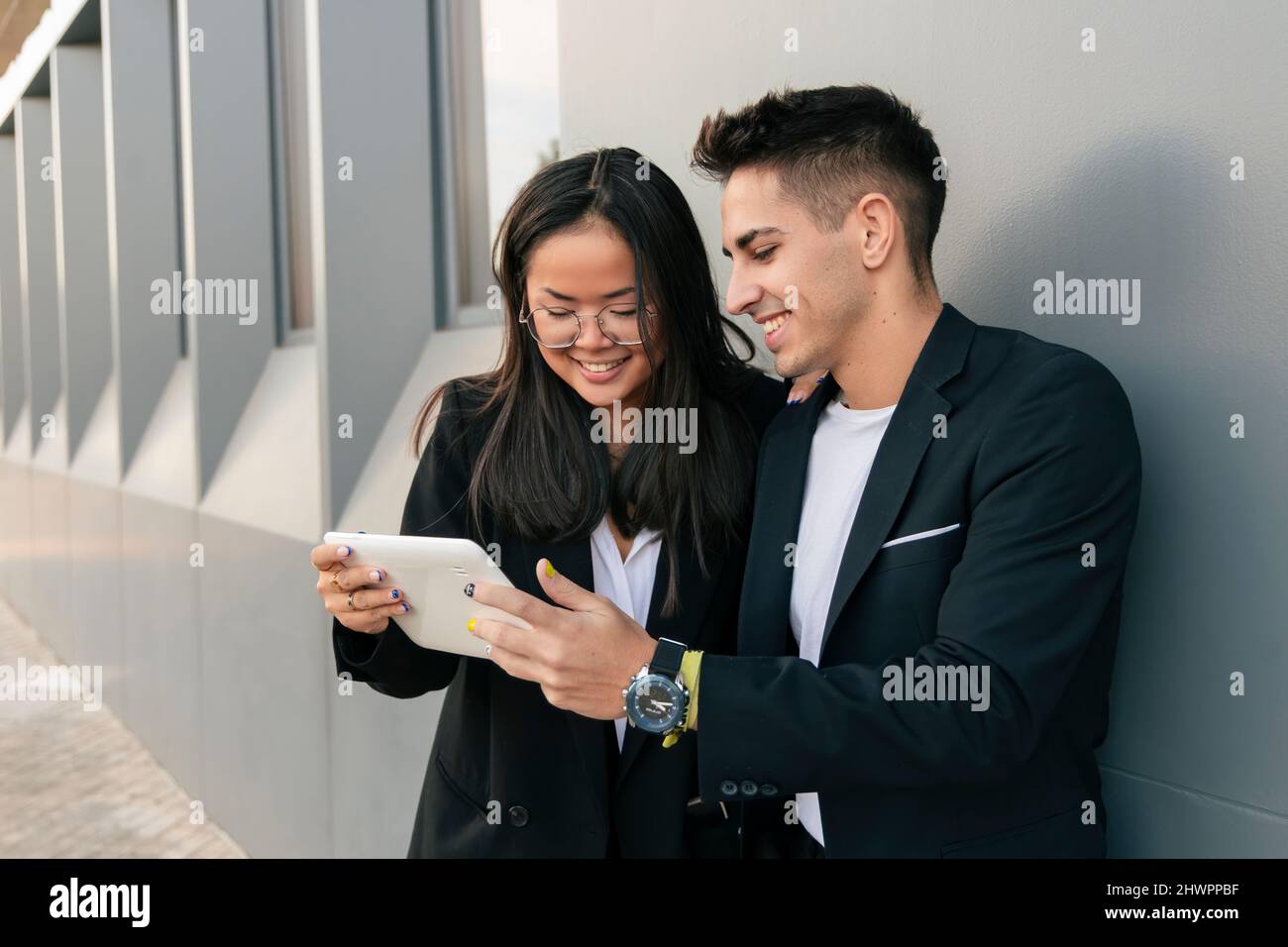 Multiracial business colleagues using tablet PC leaning on wall Stock Photo
