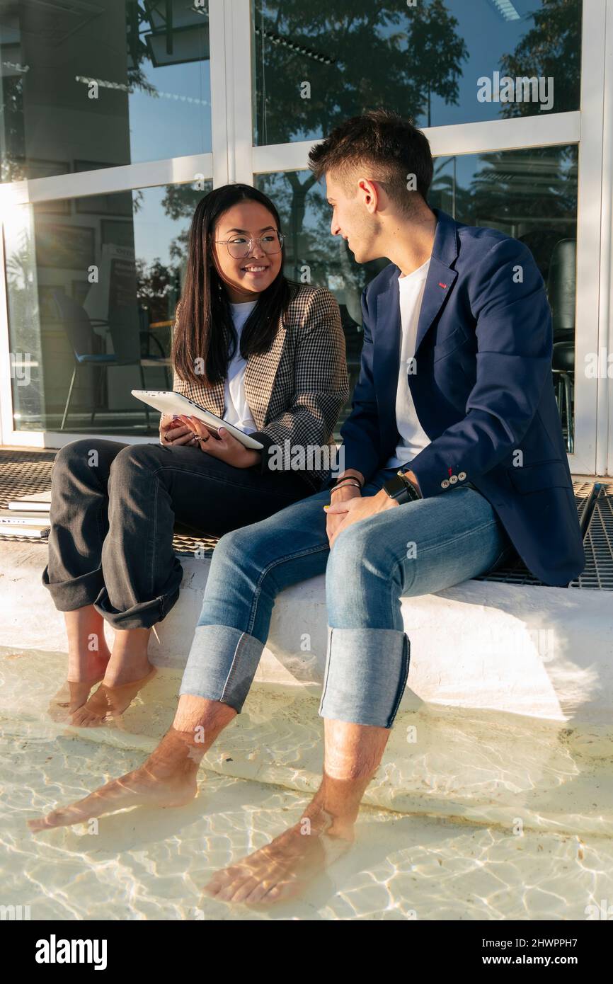 Businesswoman with tablet PC sitting by colleague at pool Stock Photo