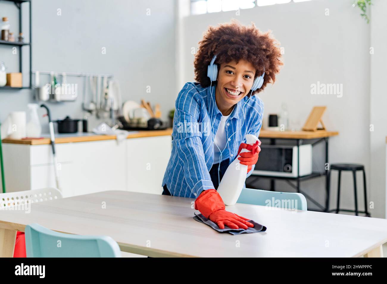 https://c8.alamy.com/comp/2HWPPPC/smiling-afro-woman-listening-music-cleaning-dining-table-in-kitchen-2HWPPPC.jpg