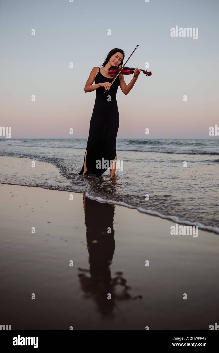 Woman playing violin standing in sea at sunset Stock Photo - Alamy