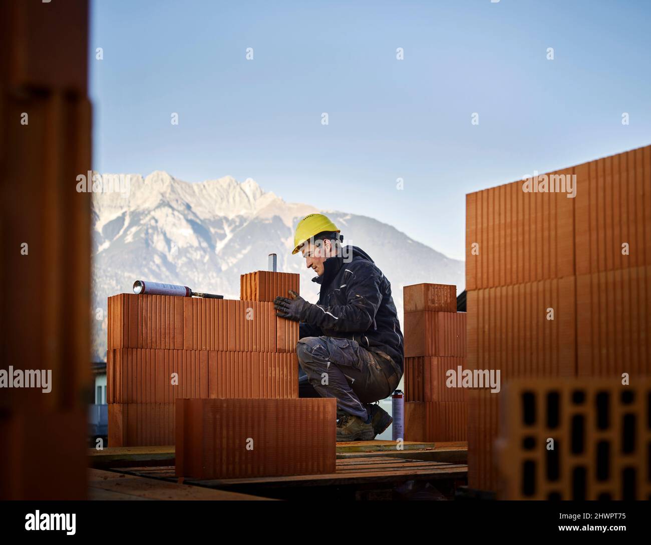 Bricklayer fixing bricks crouching at construction site Stock Photo