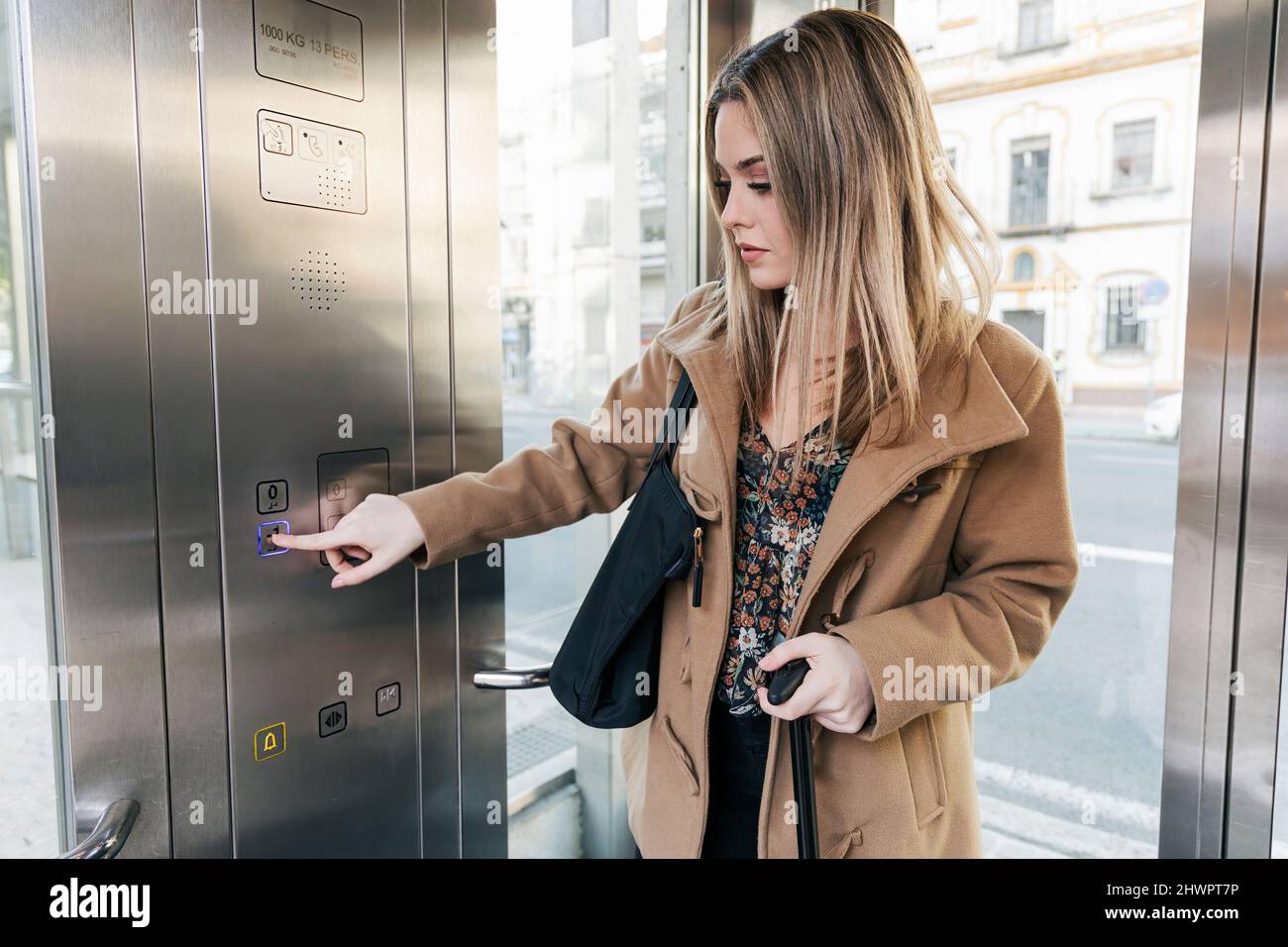 Blond woman pressing button in elevator Stock Photo