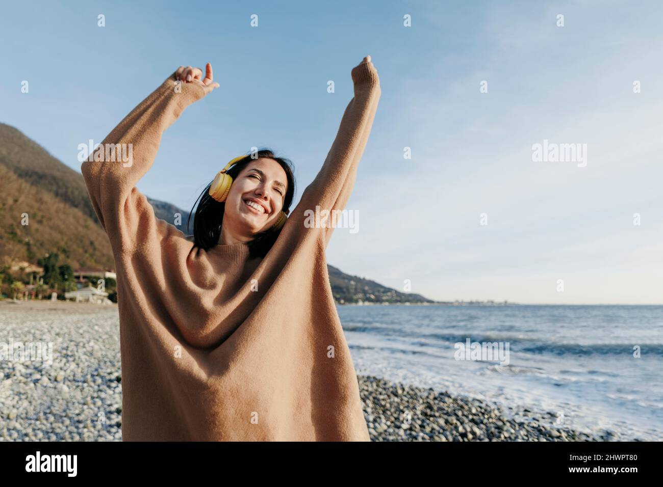 Happy young woman listening music through headphones dancing at beach ...